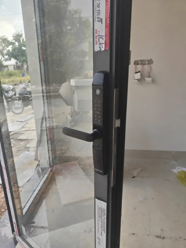 Khóa Kenitsu SA1 màu đen trên cánh cửa nhôm kính đang mở, nhìn rõ tay gạt và cạnh chốt.